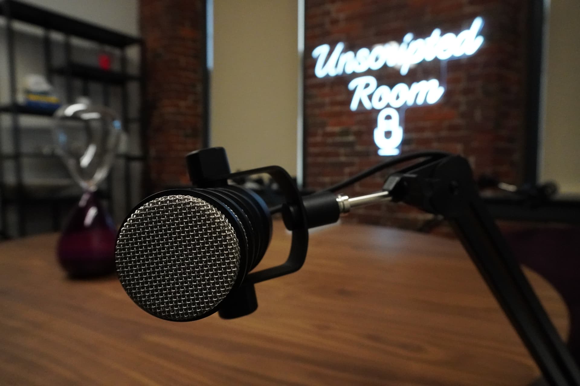 A microphone at the table inside The Unscripted Room, with the glowing Unscripted Room sign against the brick behind